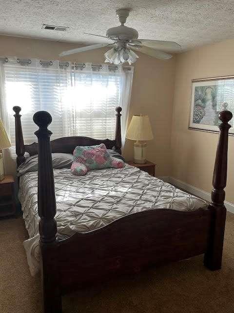 bedroom featuring a textured ceiling, carpet, visible vents, and a ceiling fan