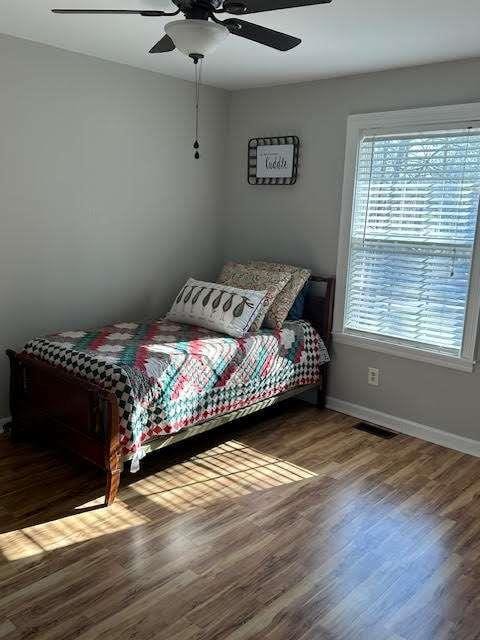 bedroom featuring ceiling fan, wood finished floors, visible vents, and baseboards