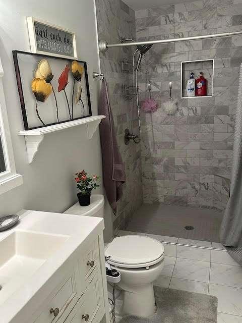 bathroom with a tile shower, vanity, and toilet