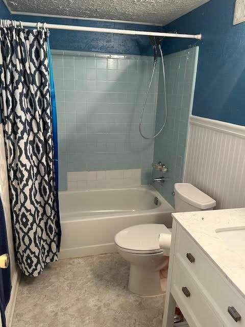 full bathroom with a textured ceiling, toilet, vanity, wainscoting, and shower / bath combo with shower curtain