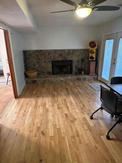 living area featuring light wood-style flooring, a fireplace, a ceiling fan, and french doors