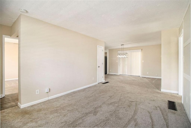 carpeted spare room featuring a textured ceiling and a chandelier