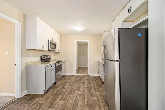 kitchen featuring dark hardwood / wood-style floors, stainless steel appliances, white cabinets, and light stone counters