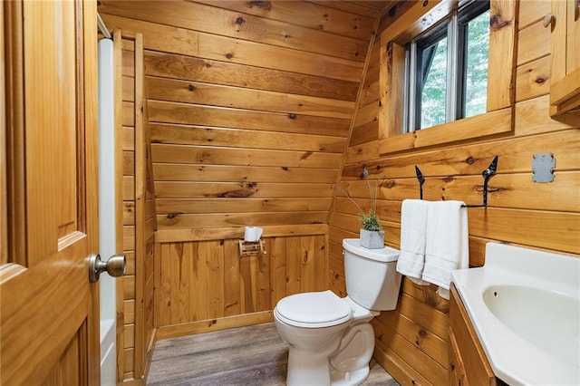 half bathroom with wood finished floors, toilet, wood walls, and vanity