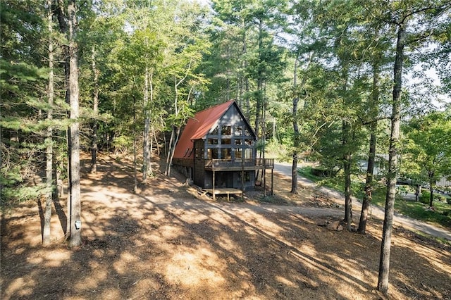 back of property featuring metal roof, a view of trees, and a wooden deck