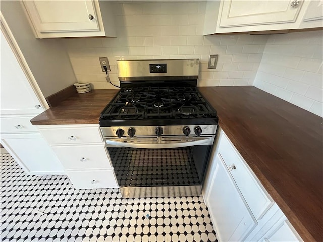 kitchen with stainless steel gas stove, butcher block counters, white cabinets, and decorative backsplash