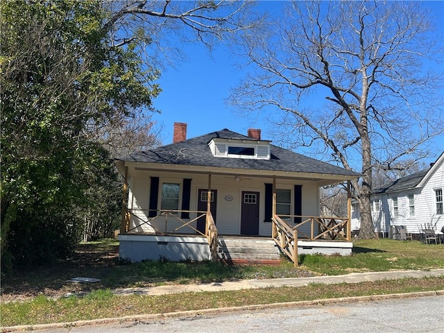 bungalow-style house featuring a shingled roof, covered porch, and a chimney