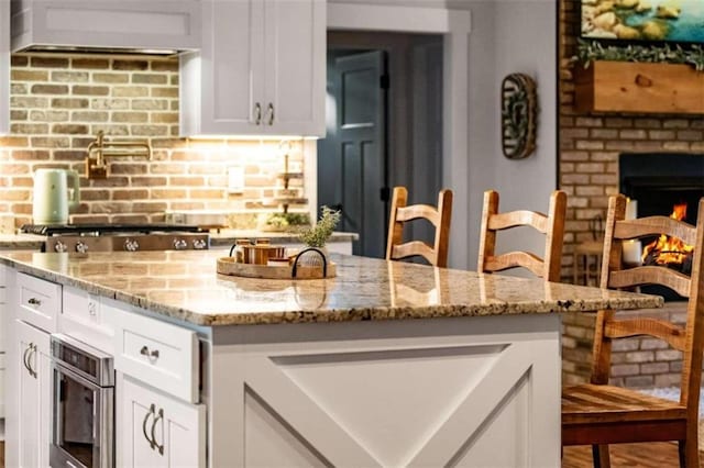 kitchen featuring white cabinetry, light stone counters, backsplash, and a fireplace