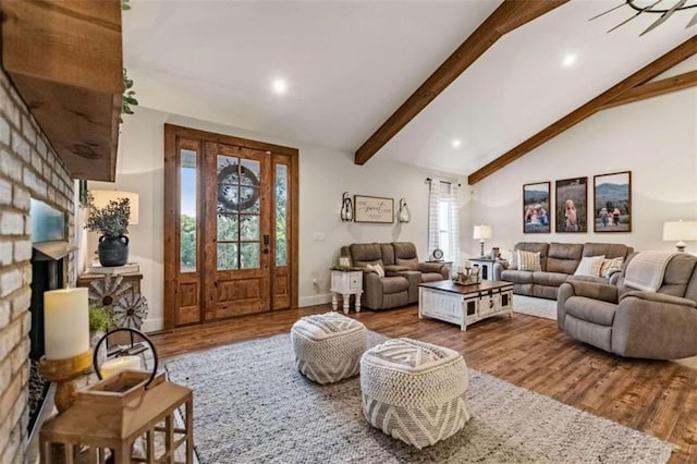 living room with lofted ceiling with beams, wood-type flooring, and a brick fireplace