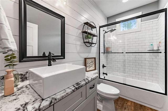 full bathroom featuring wood walls, shower / bath combination with glass door, toilet, vanity, and hardwood / wood-style flooring