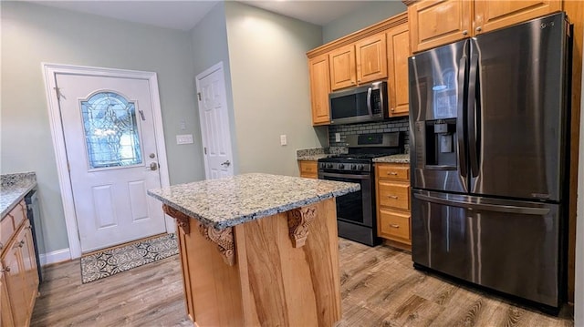 kitchen featuring a center island, backsplash, light hardwood / wood-style flooring, appliances with stainless steel finishes, and light stone counters