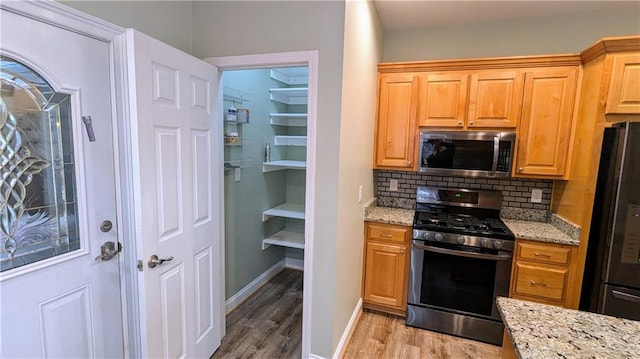 kitchen featuring tasteful backsplash, light stone counters, stainless steel appliances, and light hardwood / wood-style floors