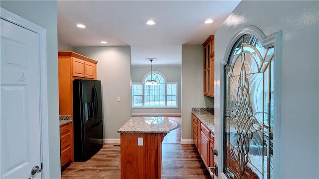 kitchen featuring black fridge, light stone counters, crown molding, light hardwood / wood-style floors, and a kitchen island