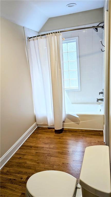 bathroom featuring toilet, wood-type flooring, vaulted ceiling, and shower / bathtub combination with curtain