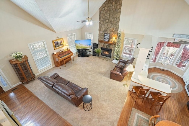 living room featuring a healthy amount of sunlight, ceiling fan, high vaulted ceiling, and a stone fireplace