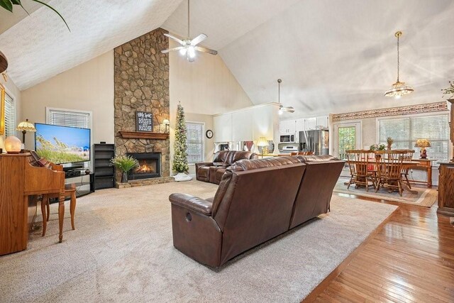 living room with ceiling fan, high vaulted ceiling, light wood-type flooring, and a stone fireplace