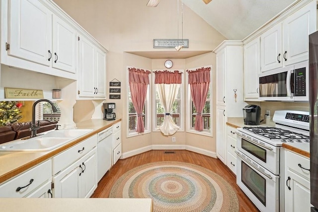 kitchen with white appliances, sink, vaulted ceiling, white cabinets, and light hardwood / wood-style flooring