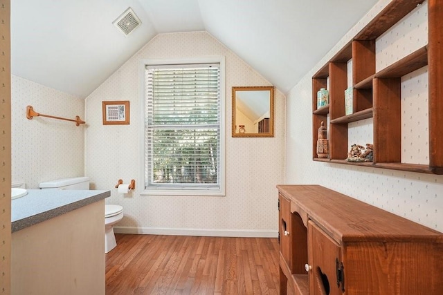 bathroom featuring toilet, wood-type flooring, vaulted ceiling, and a wealth of natural light