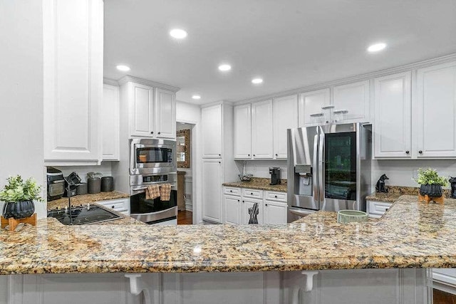 kitchen with appliances with stainless steel finishes, kitchen peninsula, white cabinetry, and light stone countertops