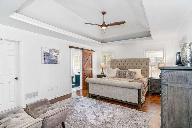 bedroom featuring dark hardwood / wood-style flooring, a barn door, ceiling fan, and a raised ceiling