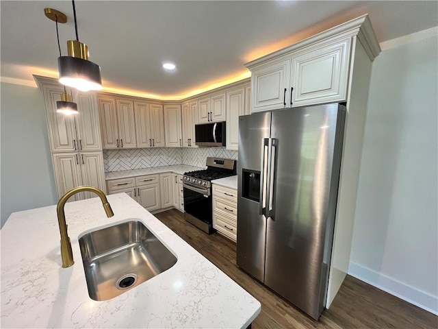 kitchen featuring light stone counters, a sink, appliances with stainless steel finishes, backsplash, and dark wood-style flooring
