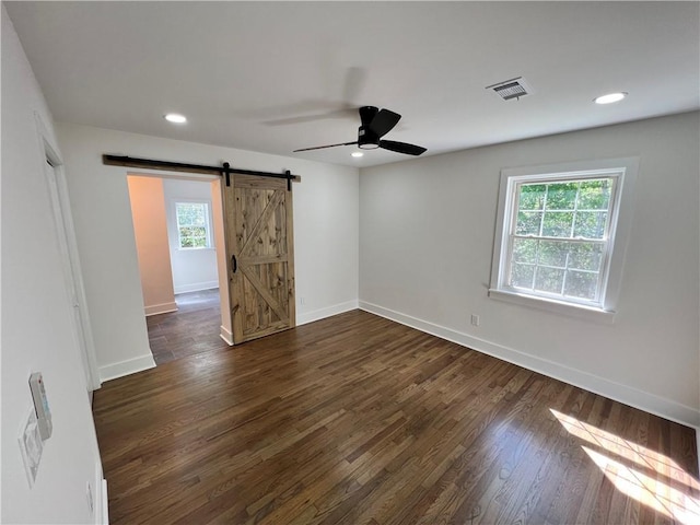 empty room featuring a ceiling fan, visible vents, a wealth of natural light, and a barn door