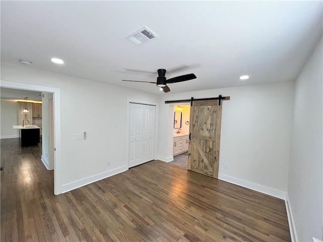 unfurnished bedroom with a barn door, baseboards, dark wood-type flooring, visible vents, and recessed lighting