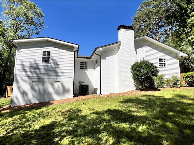 back of property with cooling unit, a lawn, and a chimney