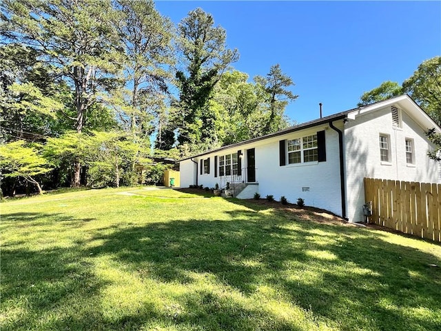 back of house with brick siding, a lawn, and fence