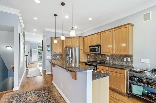 kitchen featuring appliances with stainless steel finishes, light hardwood / wood-style flooring, hanging light fixtures, and an island with sink