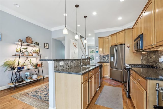 kitchen featuring sink, stainless steel appliances, crown molding, light hardwood / wood-style flooring, and a center island with sink