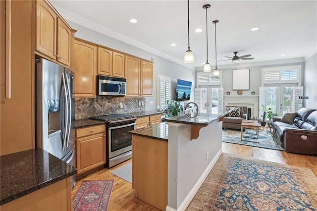 kitchen with appliances with stainless steel finishes, an island with sink, decorative light fixtures, ornamental molding, and light hardwood / wood-style flooring