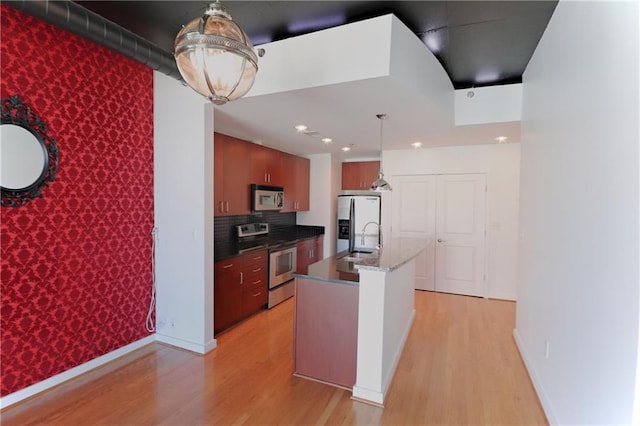 kitchen with decorative light fixtures, stainless steel appliances, light hardwood / wood-style floors, sink, and a kitchen island with sink