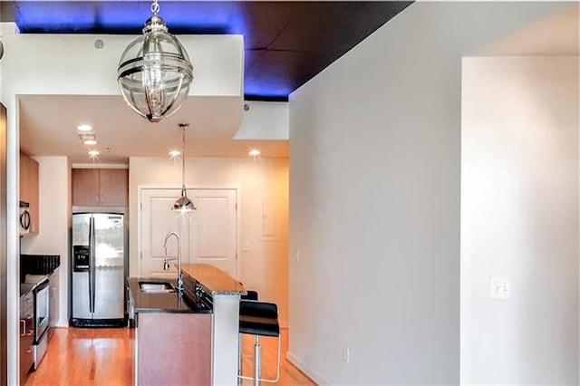 kitchen with decorative light fixtures, sink, light hardwood / wood-style flooring, a kitchen breakfast bar, and stainless steel appliances