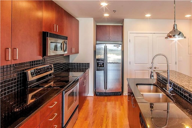 kitchen with stainless steel appliances, backsplash, light wood-type flooring, dark stone counters, and sink