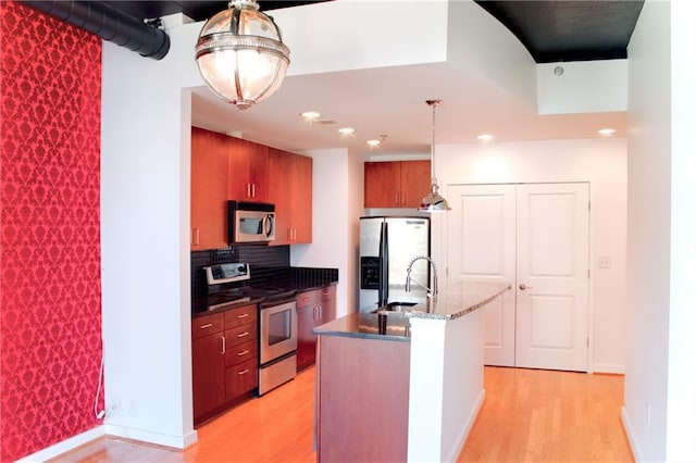 kitchen featuring decorative light fixtures, sink, light hardwood / wood-style flooring, appliances with stainless steel finishes, and an island with sink