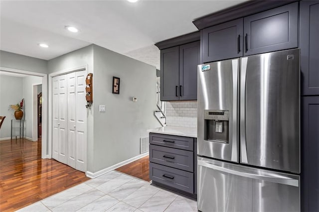 kitchen featuring light wood-type flooring, stainless steel refrigerator with ice dispenser, backsplash, and baseboards