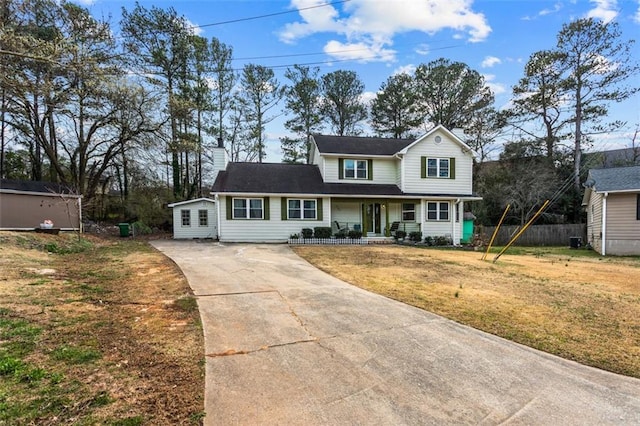 traditional home with concrete driveway, a chimney, covered porch, fence, and a front yard