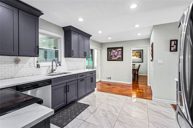 kitchen with baseboards, decorative backsplash, light stone counters, appliances with stainless steel finishes, and a sink