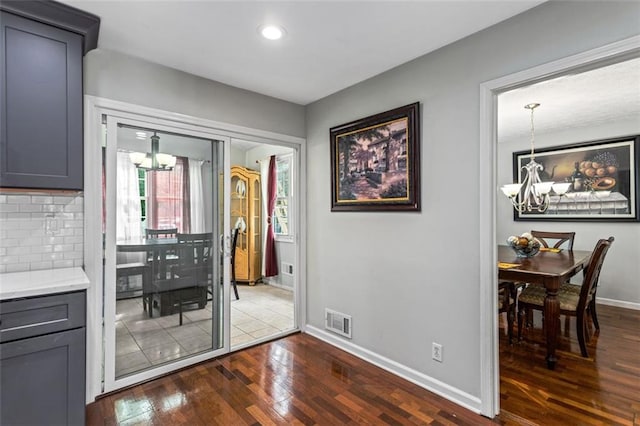 hall with dark wood-style floors, baseboards, visible vents, and a notable chandelier