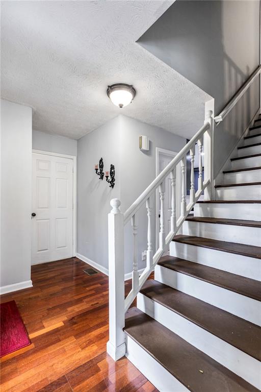 stairs with visible vents, a textured ceiling, baseboards, and wood finished floors