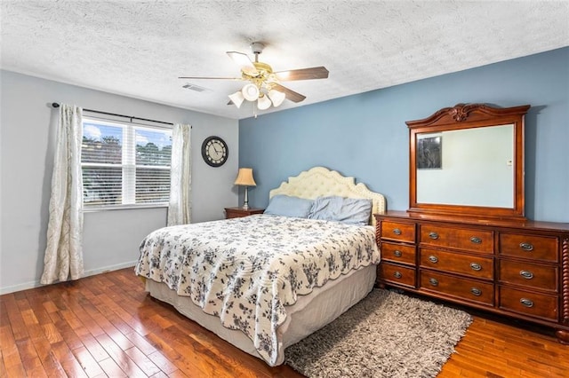 bedroom featuring wood-type flooring, visible vents, ceiling fan, a textured ceiling, and baseboards