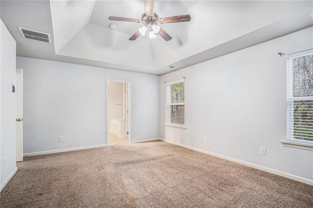 carpeted empty room with ceiling fan, vaulted ceiling, and a tray ceiling