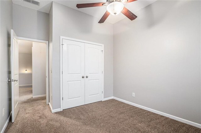 unfurnished bedroom featuring light carpet, a towering ceiling, a closet, and ceiling fan