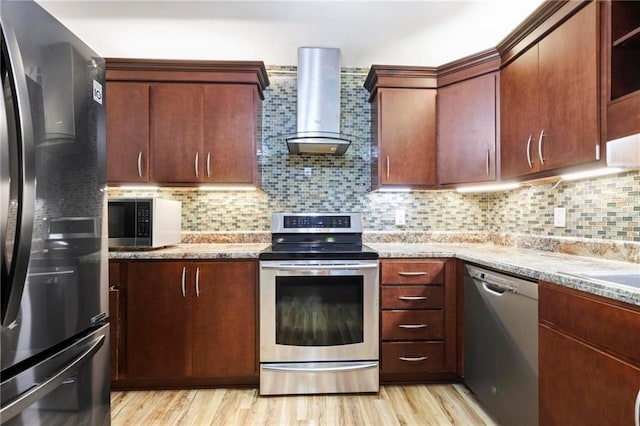 kitchen featuring appliances with stainless steel finishes, tasteful backsplash, light wood-type flooring, and wall chimney exhaust hood