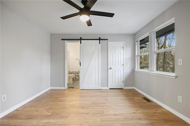 unfurnished bedroom featuring visible vents, baseboards, a barn door, light wood finished floors, and ensuite bath