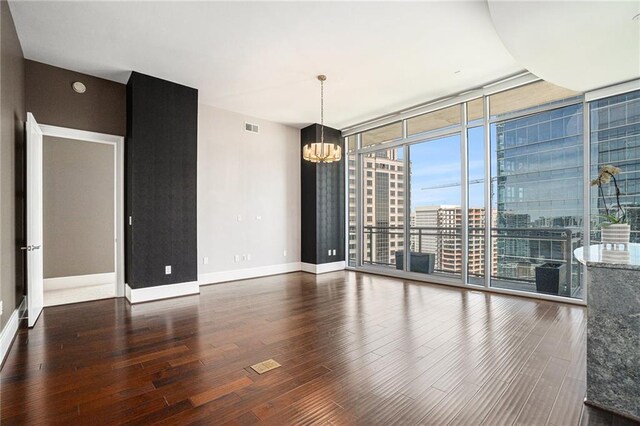 spare room featuring visible vents, wood finished floors, an inviting chandelier, a wall of windows, and baseboards
