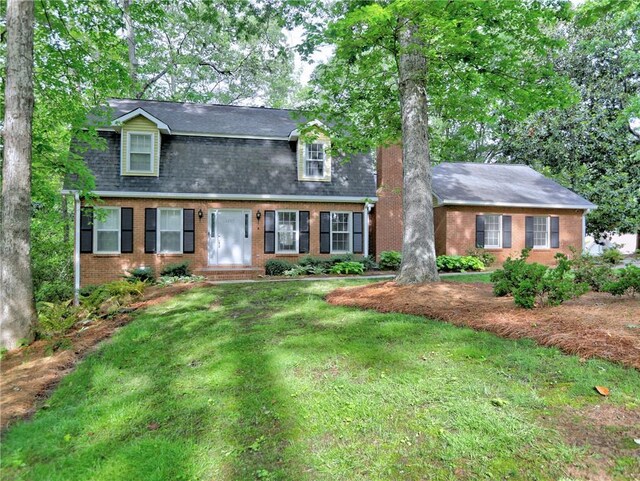 view of front of property featuring a shingled roof, a front yard, and brick siding