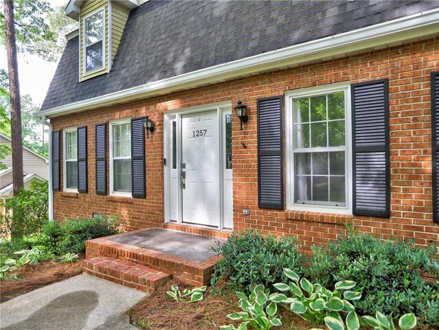 entrance to property with brick siding and a shingled roof