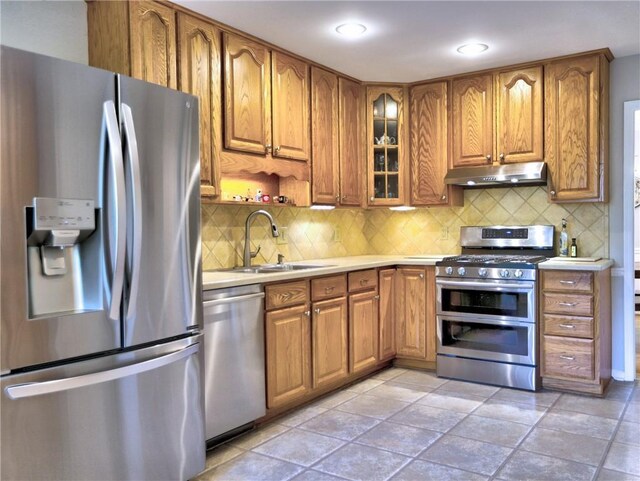 kitchen featuring appliances with stainless steel finishes, brown cabinets, a sink, light countertops, and under cabinet range hood